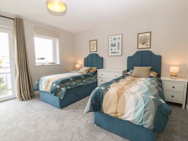 A bedroom with two single beds blue headboards patterned bedding bedside tables lamps and framed pictures on the wall at 1 Crud Y Mor in Barmouth