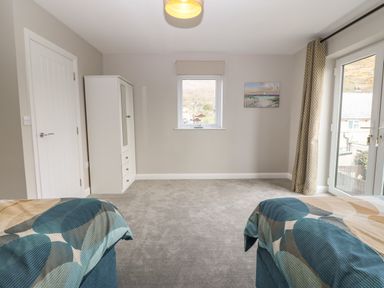 A bedroom with two beds a wardrobe a window and glass doors at 1 Crud Y Mor in Barmouth