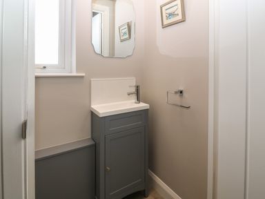 A small bathroom with a grey sink cabinet mirror above the sink and a towel rack on the wall at 1 Crud Y Mor in Barmouth