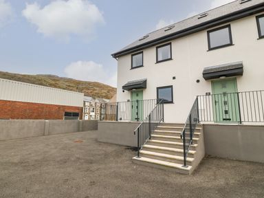 Entrance steps leading to two doors of a modern building with black railings and surrounding paved area at 1 Crud Y Mor in Barmouth