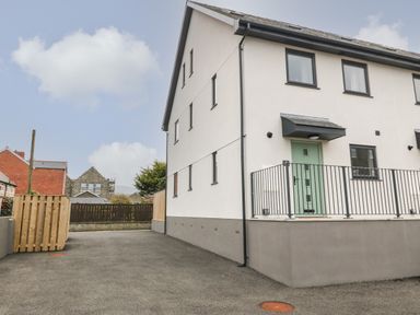 The exterior of a modern two-story house with a green door and fenced area at 1 Crud Y Mor in Barmouth