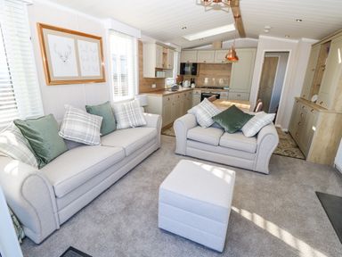 A living room with two sofas and an ottoman next to a kitchen area at Vendee Lodge Thorness Bay Holiday Park near Cowes
