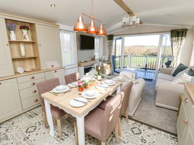 An open dining and living area with a table set for four chairs and sofas overlooking a balcony with countryside views at Vendee Lodge Thorness Bay Holiday Park near Cowes