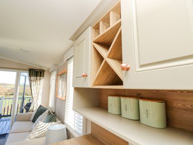 Kitchen cabinets with three labeled containers and a living area with sofa and windows at Vendee Lodge Thorness Bay Holiday Park near Cowes