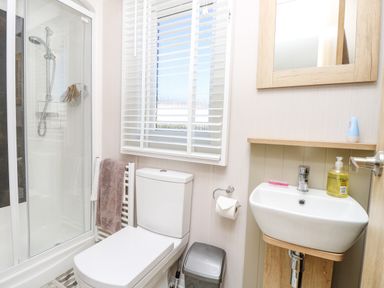 A bathroom with a shower cubicle a toilet a sink with a mirror and a window with blinds at Vendee Lodge Thorness Bay Holiday Park near Cowes