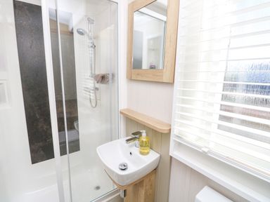 A bathroom with a glass shower enclosure a white sink and a wall mirror at Vendee Lodge Thorness Bay Holiday Park near Cowes