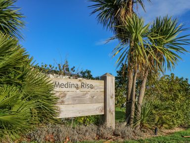 A wooden sign reading Medina Rise surrounded by plants and trees under a blue sky