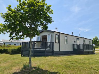 A mobile home with a wooden deck and a tree in the yard at Vendee Lodge Thorness Bay Holiday Park near Cowes