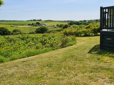 A grassy area with bushes and trees with fields and farm buildings in the distance at Vendee Lodge Thorness Bay Holiday Park near Cowes