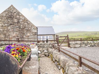 A stone building with a gravel pathway and colorful flowers in planters at Caerffynon Bach in Dyffryn Ardudwy