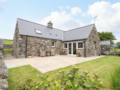 A stone cottage with a tiled roof patio area and garden at Caerffynon Bach in Dyffryn Ardudwy