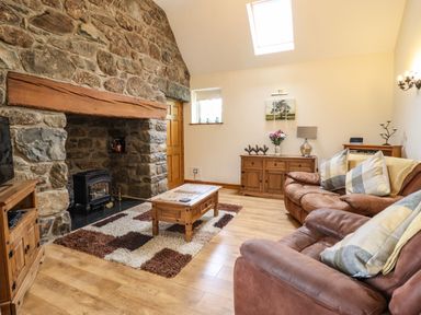 A living room with stone fireplace wooden furniture sofas and a skylight at Caerffynon Bach in Dyffryn Ardudwy