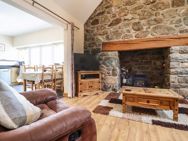 A living room with a stone fireplace wooden coffee table and television next to a dining area at Caerffynon Bach in Dyffryn Ardudwy