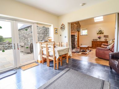 A dining area with a table and chairs leading to a living room with sofas and a stone fireplace at Caerffynon Bach in Dyffryn Ardudwy