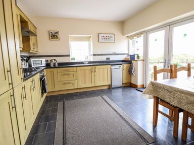 A kitchen with wooden cabinets a dining table with chairs and glass doors at Caerffynon Bach in Dyffryn Ardudwy