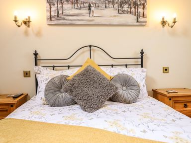 A bed with floral bedding and round and square cushions between two wooden bedside tables at Caerffynon Bach in Dyffryn Ardudwy