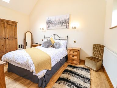 A bedroom with a bed side tables a wardrobe a chair a floor mirror and a striped rug at Caerffynon Bach in Dyffryn Ardudwy