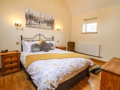 A bedroom with a bed a wooden nightstand a chair and a window at Caerffynon Bach in Dyffryn Ardudwy
