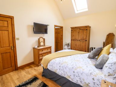 A bedroom with a bed, wooden dresser, wardrobe, wall-mounted TV, and skylight at Caerffynon Bach in Dyffryn Ardudwy