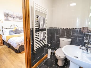 A bathroom with a toilet sink towel rack and striped towels next to a bedroom with a bed and pillows at Caerffynon Bach in Dyffryn Ardudwy