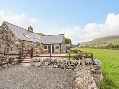 A stone cottage with a slate roof and a fenced patio area next to a green field at Caerffynon Bach in Dyffryn Ardudwy