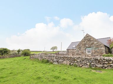 A stone house with a slate roof and a stone wall surrounding a green grassy area at Caerffynon Bach in Dyffryn Ardudwy