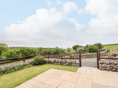 An outdoor patio area with stone paving and grass surrounded by low stone walls and wooden fencing at Caerffynon Bach in Dyffryn Ardudwy