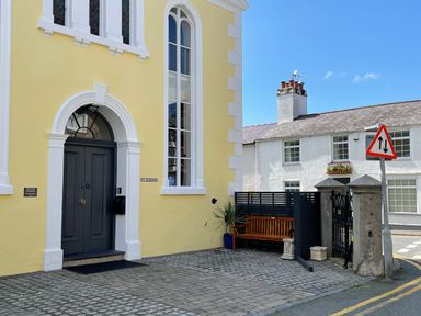 A yellow building with a dark door and tall windows next to a bench and a traffic sign at Ty Biwmares in Beaumaris