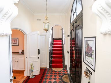 An entry hallway with a red carpeted staircase black front door a hanging light fixture and a framed picture on the wall at Ty Biwmares Beaumaris