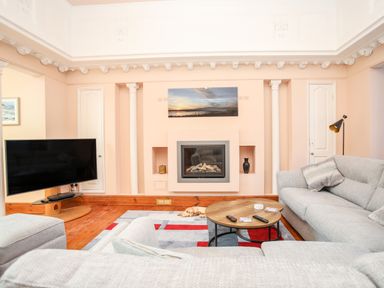 A living room with two grey sofas a round wooden coffee table a fireplace and a wall-mounted television at Ty Biwmares in Beaumaris