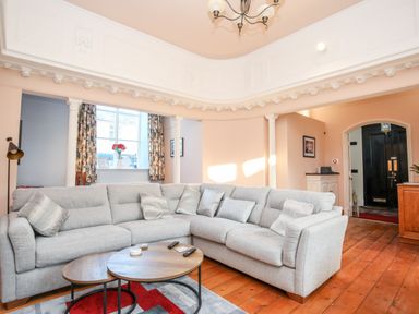 A living room with a grey sectional sofa wooden floor and round nesting coffee tables at Ty Biwmares in Beaumaris