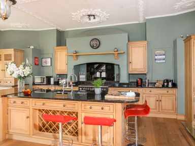 A kitchen with wooden cabinets black countertops and red bar stools at Ty Biwmares in Beaumaris