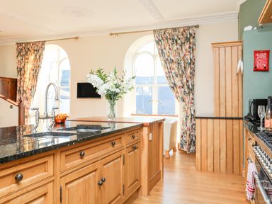 A kitchen with wooden cabinets black countertops a vase of white flowers and floral curtains at Ty Biwmares in Beaumaris