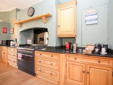 A kitchen with wooden cabinets black countertop a stove microwave and kettle at Ty Biwmares in Beaumaris