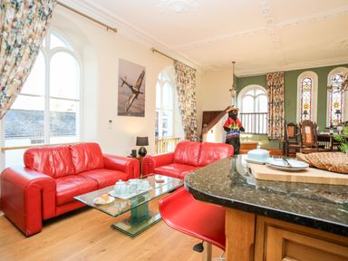 A living room with red leather sofas glass coffee table and stained glass windows at Ty Biwmares in Beaumaris