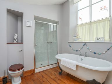 A bathroom with clawfoot bathtub and shower enclosure by a window at Ty Biwmares in Beaumaris