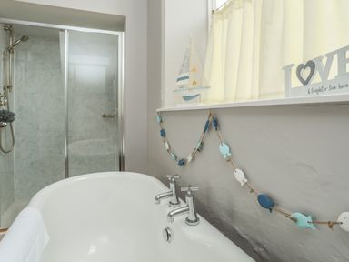 A bathroom with a white bathtub metal faucets a glass shower enclosure and a window shelf with decorative sailboat and love sign at Ty Biwmares in Beaumaris