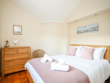 A bedroom with a wooden bed and chest of drawers pink pillows and towels on the bed at Ty Biwmares in Beaumaris