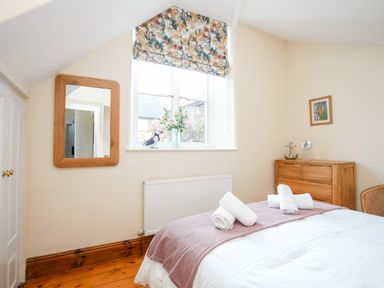 A bedroom with a bed with rolled towels window with floral blind wooden dresser and wall mirror at Ty Biwmares in Beaumaris