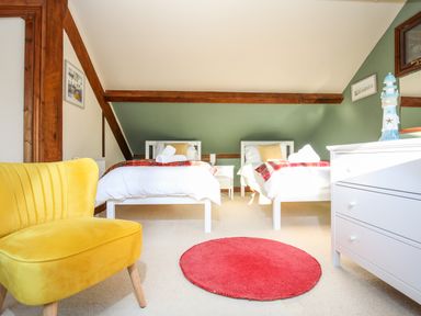 A bedroom with two single beds a yellow chair a red round rug and a white dresser at Ty Biwmares in Beaumaris