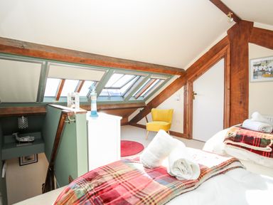 A bedroom with a yellow chair two beds with plaid blankets skylight windows and wooden beams at Ty Biwmares in Beaumaris