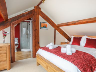 A bedroom with a bed with red pillows and a red throw and an open door showing a bathroom with a shower at Ty Biwmares in Beaumaris