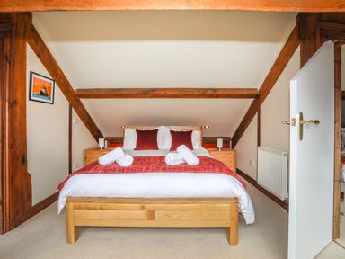 A bedroom with a double bed with red cushions and a red runner with wooden side tables and a white door at Ty Biwmares in Beaumaris