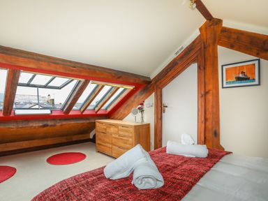 A bedroom with a bed covered with a red blanket and white towels near a wooden dresser and slanted windows at Ty Biwmares in Beaumaris