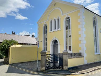 A yellow building with arched windows and a black gate at Ty Biwmares in Beaumaris