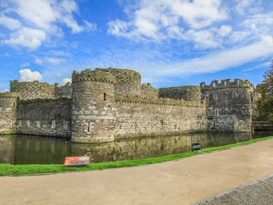 A stone castle surrounded by a water moat with a pathway and grass at Ty Biwmares in Beaumaris