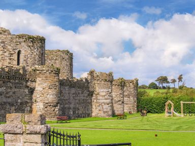 A stone castle wall with towers benches on a grassy lawn and a playground in the background at Ty Biwmares in Beaumaris