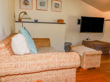 A sitting area with wicker furniture including a sofa and ottoman a wall-mounted television and framed pictures at Periwinkle Atlantic Highway near Bude
