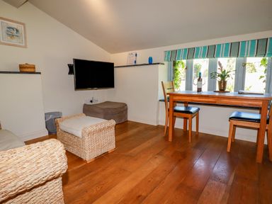 A small living area with wicker furniture a wall-mounted TV a wooden dining table with two chairs and a window with a striped blind at Periwinkle Atlantic Highway near Bude
