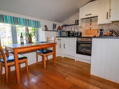 A kitchen with a wooden table and two chairs and appliances on the countertop at Periwinkle Atlantic Highway near Bude